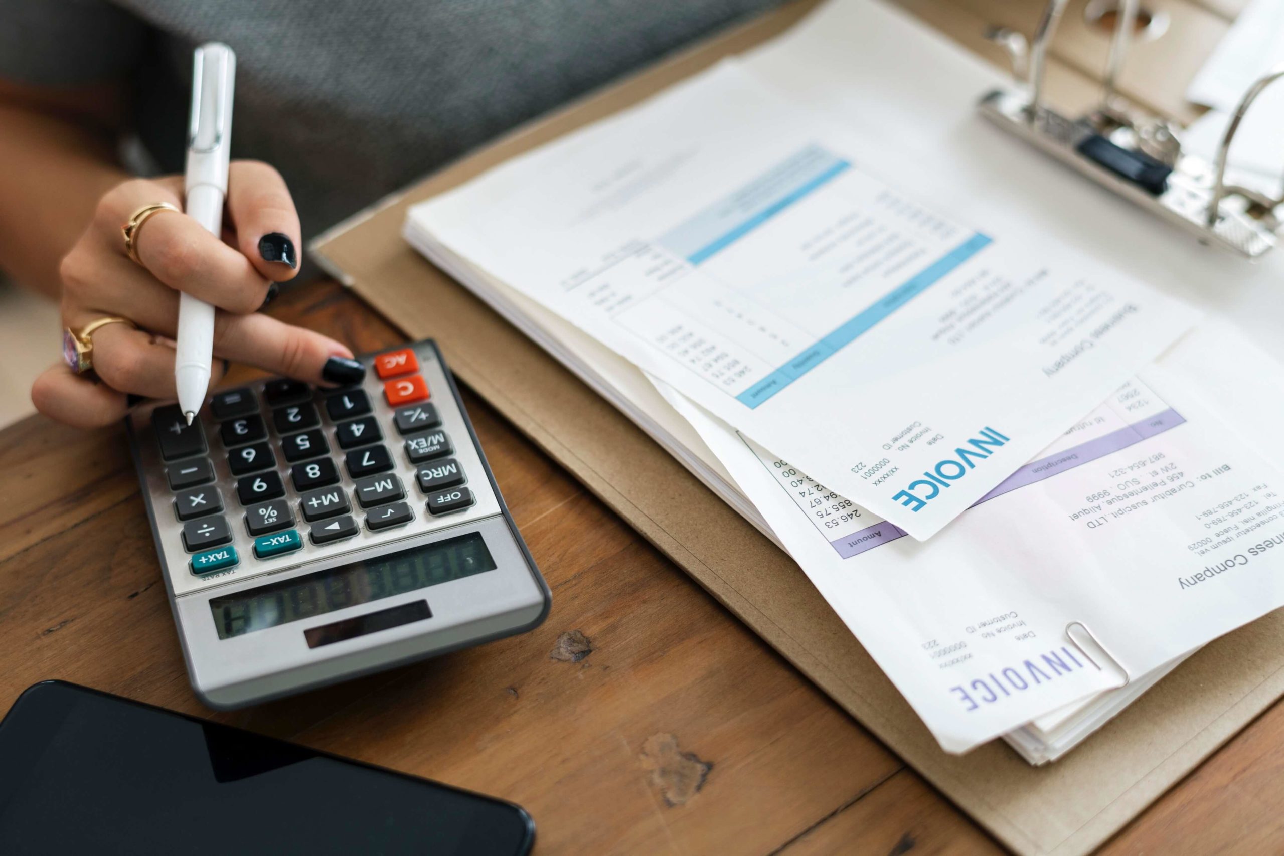 Lady with black fingernails holding a pen and typing on a calculator with invoices sitting on the desk in front of her