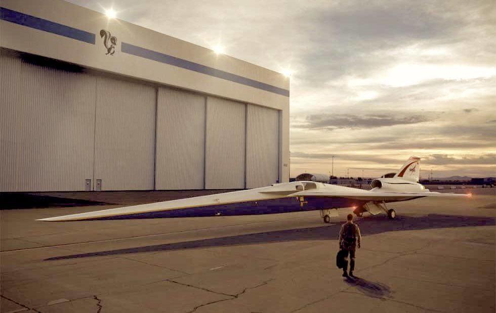 Aircraft in front of Lockheed Martin hangar at dawn with skunkworks logo, pilot walking towards the aircraft