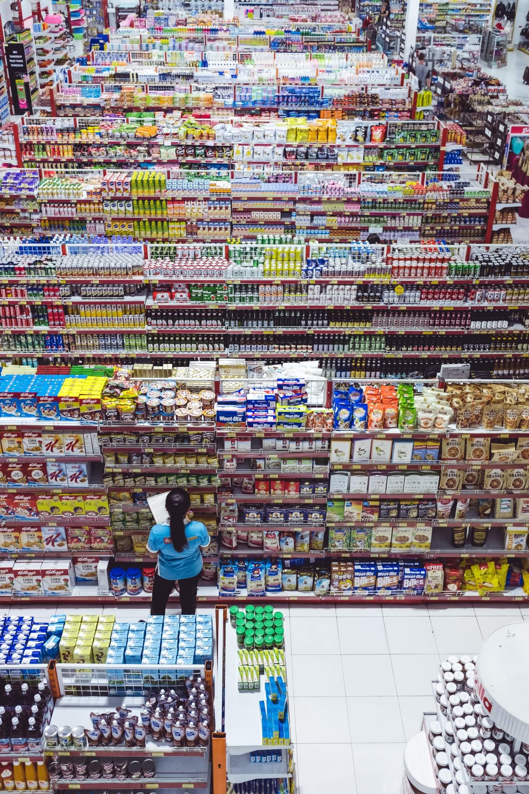 View of store shelves packed with products and clerk int he foreground checking labels