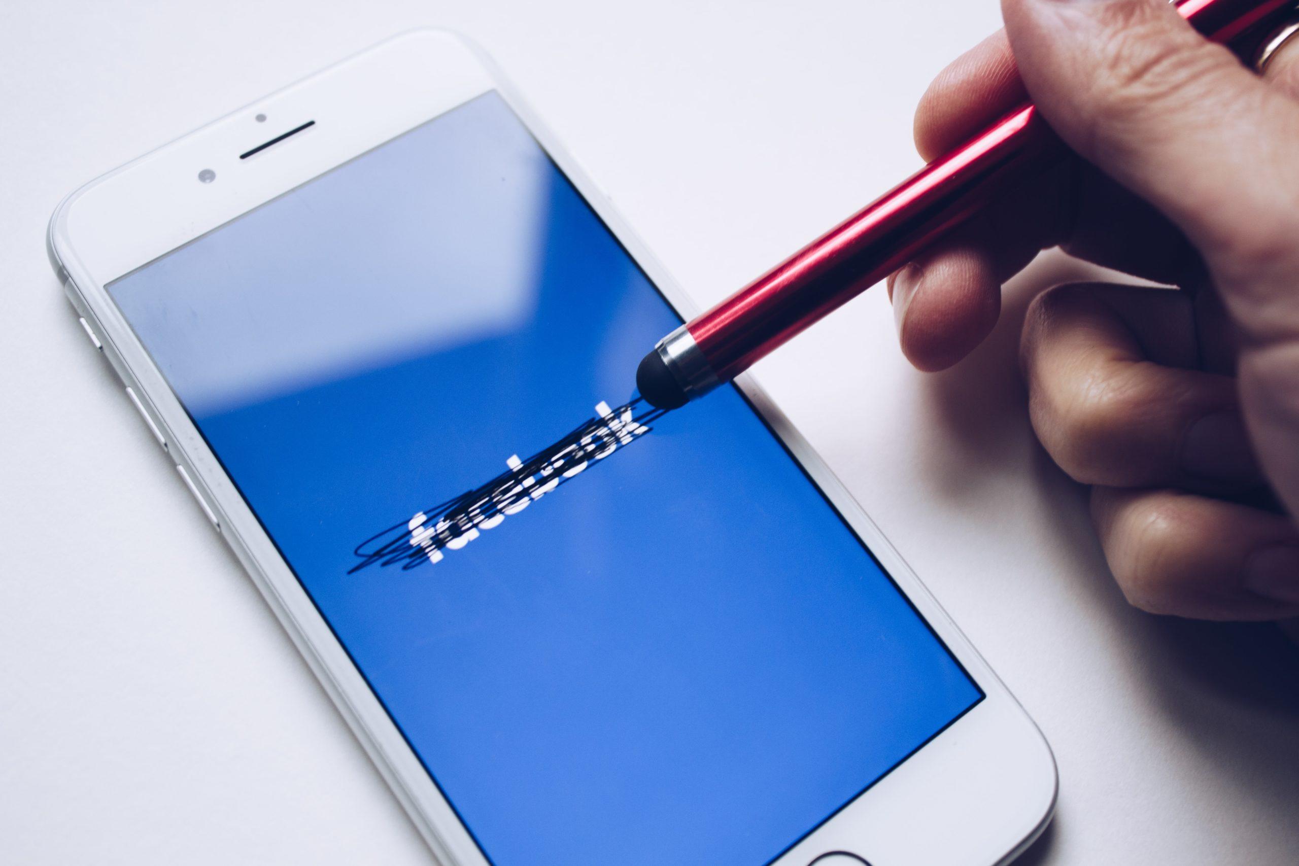 Smart phone loading Facebook with a pen eraser scratching out the logo as if in an attempt to erase